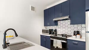 Une cuisine moderne avec des meubles de couleur bleu foncé, un plan de travail blanc, un évier en acier inoxydable et un four à micro-ondes.