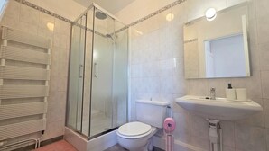 Moderni kylpyhuone, jossa on lasiseinällä varustettu suihku, wc, pesuallas ja peili.