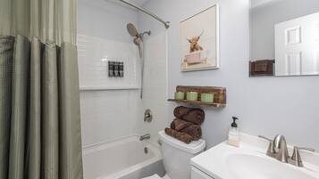 Een badkamer met een bad, toilet en wastafel. Handdoeken en toiletartikelen liggen op de muur.