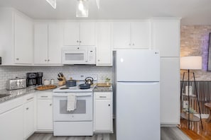 A modern kitchen with white cabinets, a microwave, an oven, a refrigerator, and a coffee maker.