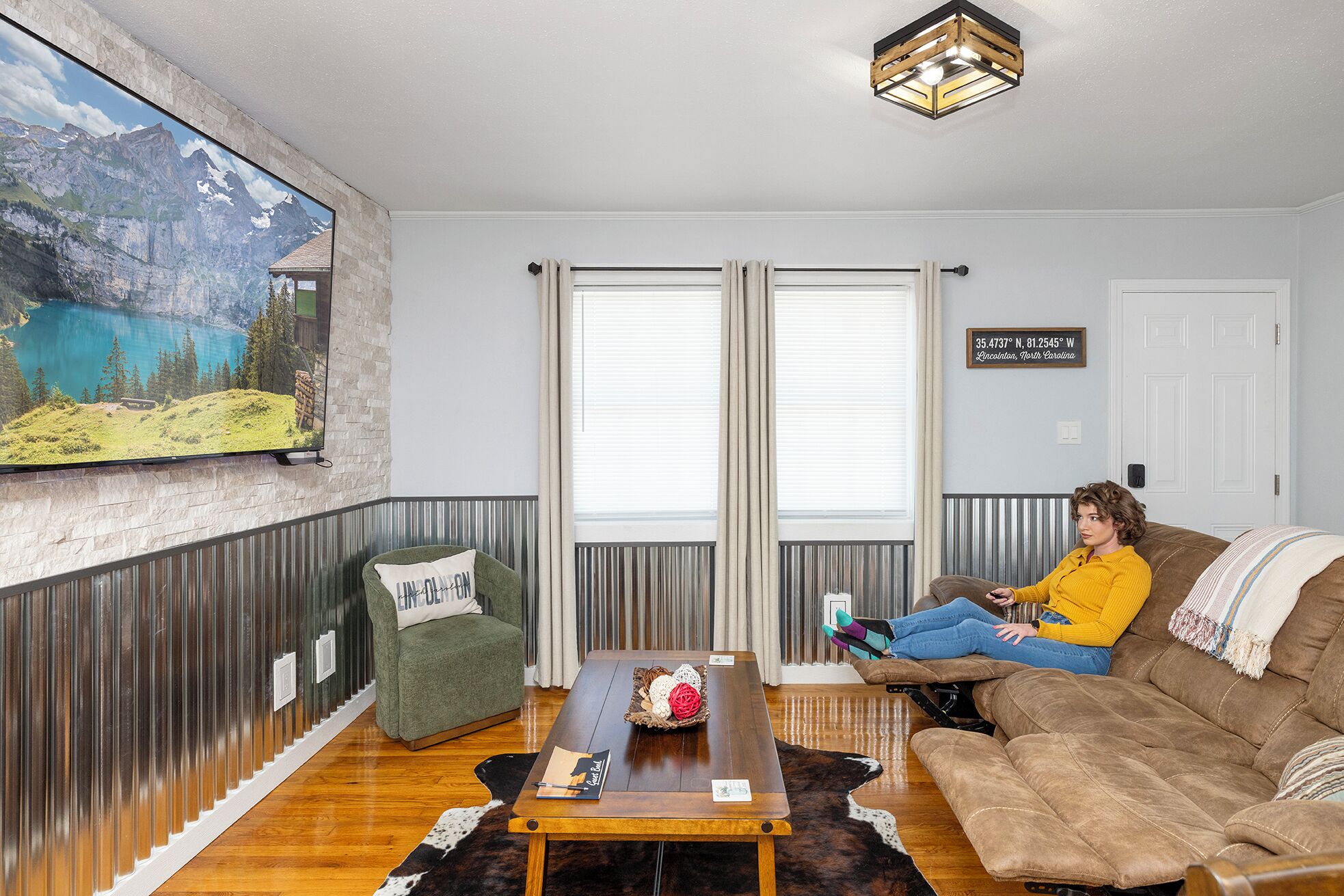 Ein Wohnzimmer mit einem großen Gemälde einer Berglandschaft, einem grünen Sessel, einem braunen Sofa und einem Holztisch.
