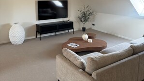 Un salon moderne avec un grand téléviseur à écran plat, un canapé beige, une table basse et une plante en pot.