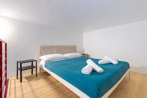 A single bed with a teal bedspread, white pillows, and rolled towels on the side. - Red Loft Torino, A mix of history and trend (Torino)