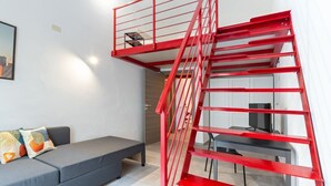 A modern interior with a red metal staircase, a grey sofa, and a dining area.