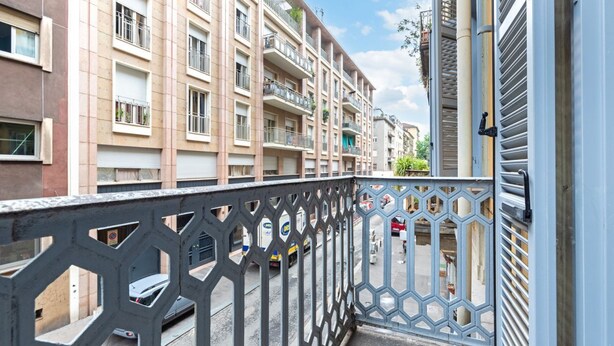 A residential building with multiple balconies, a gated entrance, and a street view.