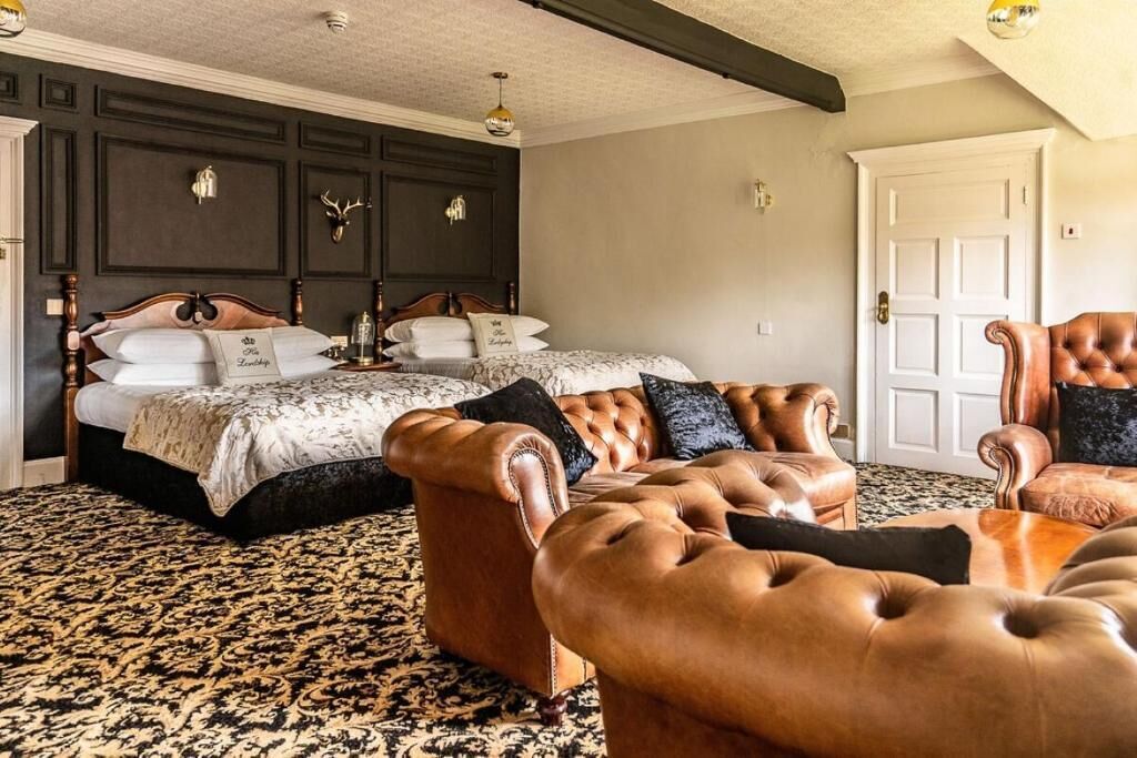 A bedroom with a large bed, two leather armchairs, a patterned carpet, and a dark wooden headboard.