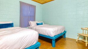 Una habitación con dos camas, una silla de madera y una cortina a cuadros.