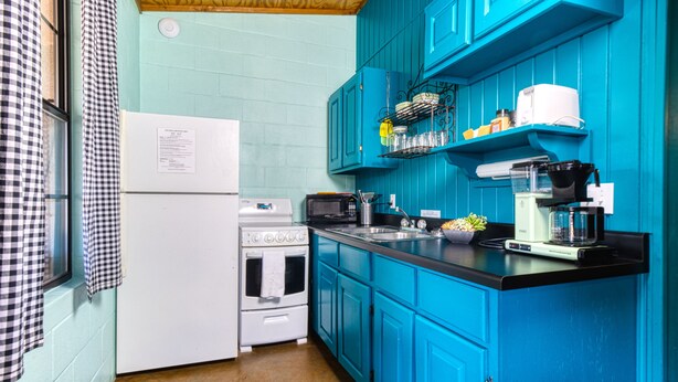Una cocina con gabinetes color turquesa, un refrigerador blanco, una estufa, un microondas y una cafetera.