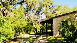 Un espacio al aire libre cubierto, con paredes de piedra, rodeado de árboles y vegetación.