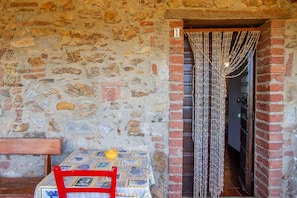 A stone wall with a brick archway, a table with a patterned tablecloth, and a red chair.