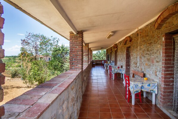 Una terraza al aire libre techada con paredes de ladrillo, sillas y mesas rojas.