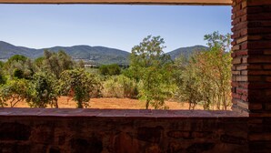 A view through a window with a stone wall, a brick wall, and a landscape with trees and hills.