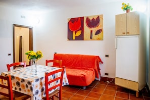 Ein Essbereich mit Tisch, Stühlen, einer Couch, einem Kühlschrank und einer Wand mit einem Blumenbild.