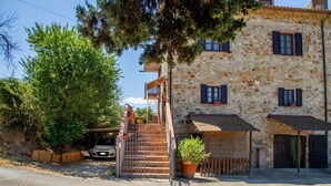 A stone building with a staircase leading to a door, a parked car, and a potted plant.