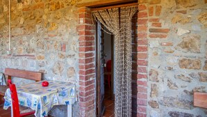 A stone-walled room with a wooden bench, a table with a patterned tablecloth, and a door with a curtain.