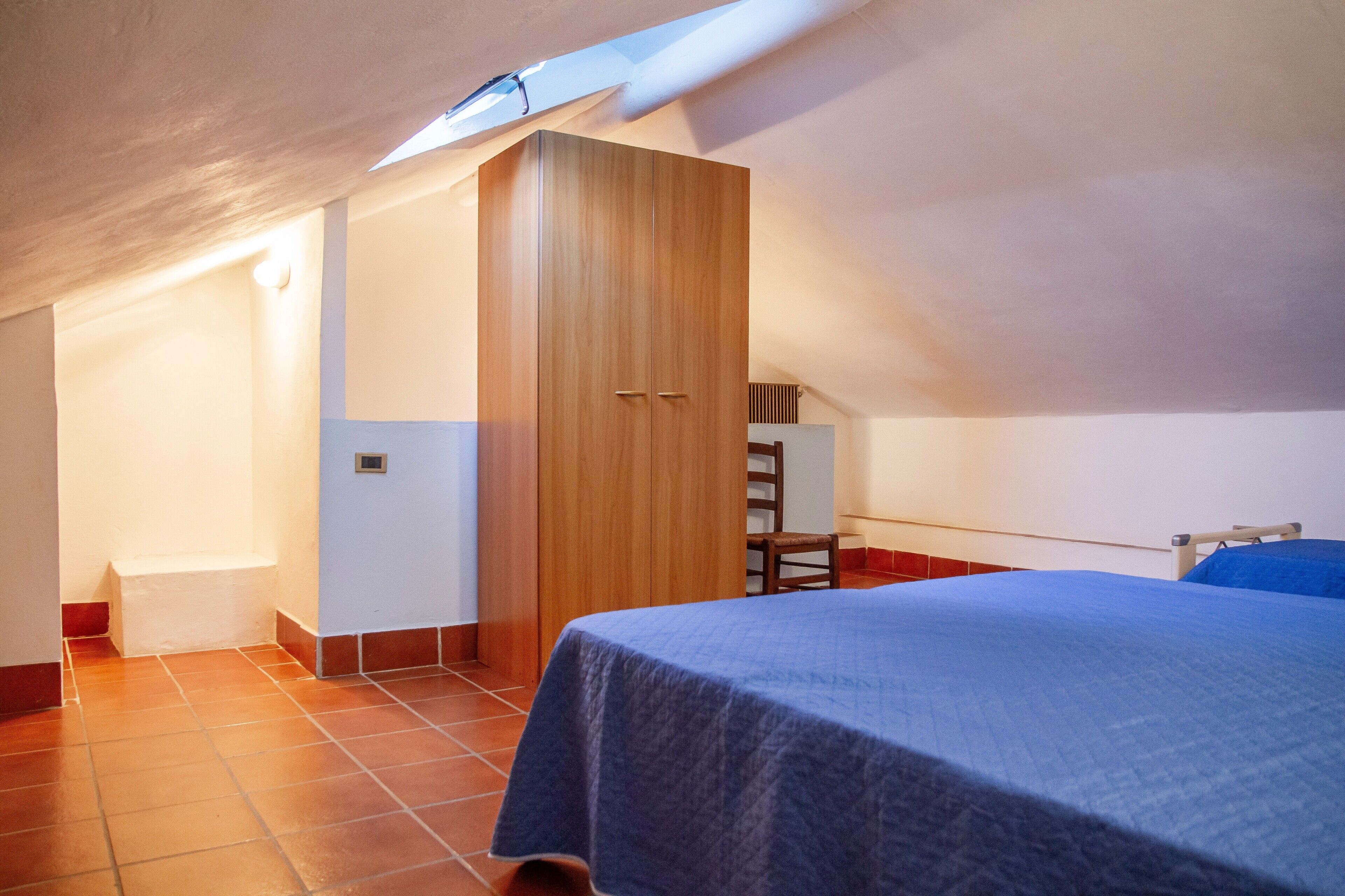 A bedroom with a bed, a wooden wardrobe, a chair, and a sloped ceiling.
