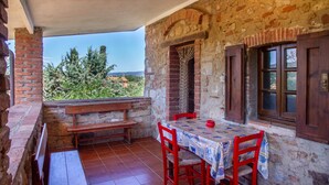 Una habitación con paredes de piedra, una mesa y sillas de madera, un banco y vistas al verdor.