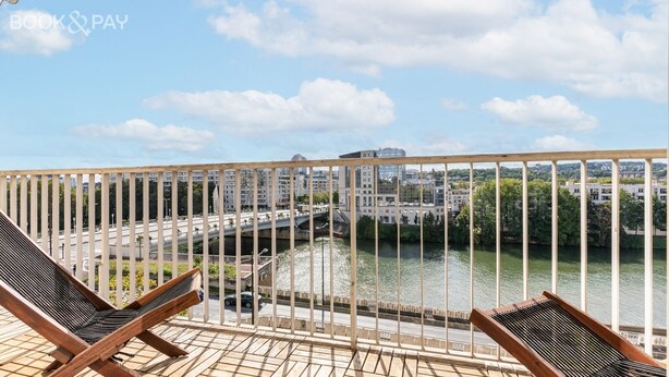 A balcony with a view of a river, a bridge, and buildings in the background.