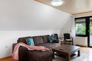 Un salon avec un canapé marron, deux fauteuils, une table basse et une grande fenêtre donnant sur un beau paysage.