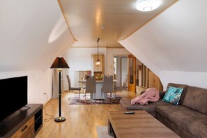 Un salon moderne avec un téléviseur à écran plat, un lampadaire, un canapé agrémenté d’un coussin décoratif et, au fond, un coin repas.