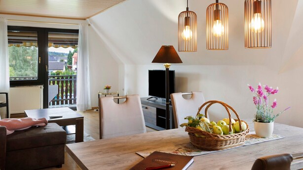 A dining area with a table, chairs, a basket of fruit, a potted plant, and pendant lights. - Apartment 'Gundlach' with Shared Terrace, Shared Garden and Wi-Fi (Hessisch Lichtenau)