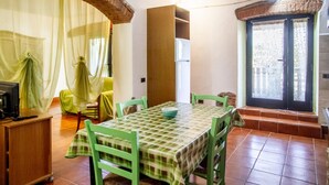 A dining area with a table, chairs, a refrigerator, and a window with a view. - Apartment 'Taverna' with Private Terrace, Shared Garden and Wi-Fi (Gavorrano)