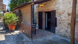 A rustic outdoor seating area with a wooden table and chairs, a potted plant, and a stone wall. - Apartment 'Taverna' with Private Terrace, Shared Garden and Wi-Fi (Gavorrano)