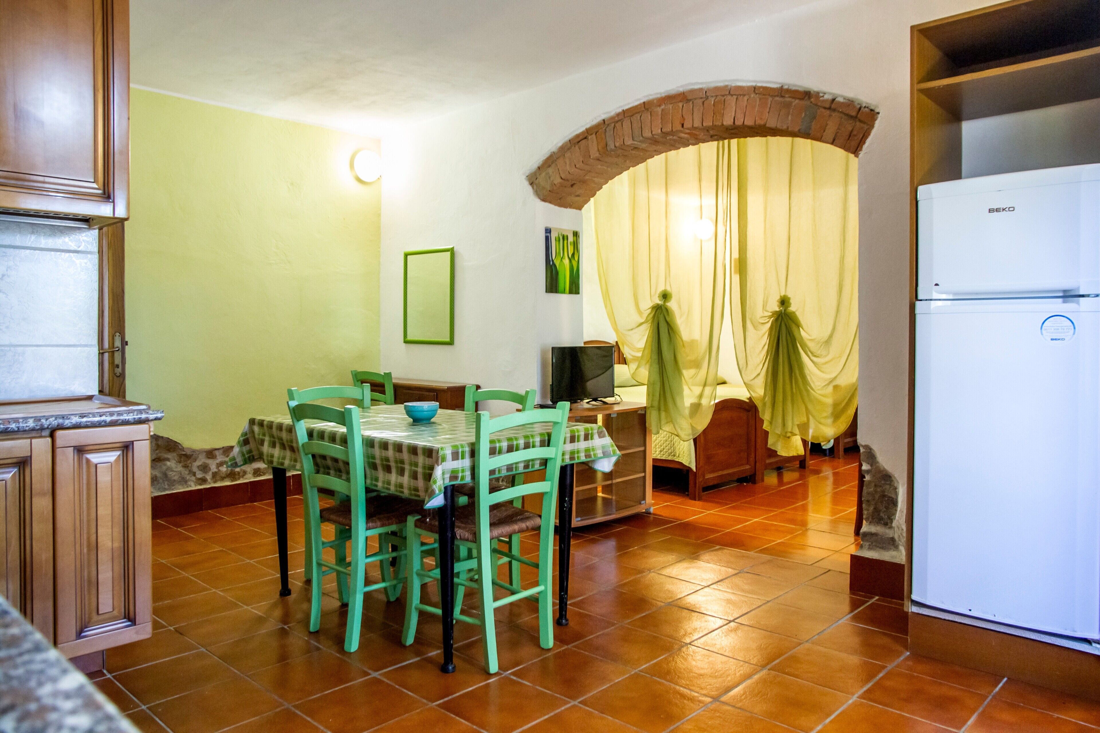 A kitchen with a dining table, chairs, a refrigerator, and a TV.