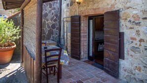 A rustic outdoor patio with a wooden table and chair, a potted plant, and a stone wall. - Apartment 'Taverna' with Private Terrace, Shared Garden and Wi-Fi (Gavorrano)