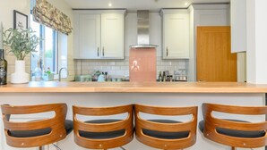 Una cocina moderna con armarios blancos, encimera de madera y cuatro taburetes de bar de madera.