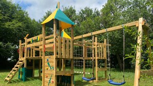 Une structure de jeux en bois comprenant un mur d’escalade, des toboggans et des balançoires.