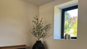 Une pièce avec une grande fenêtre, un vase noir orné de branches, un banc en bois et deux poufs ronds posés sur un tapis à motifs.