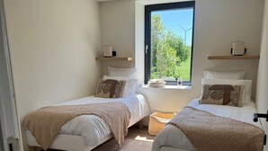 Une chambre avec deux lits, une grande fenêtre et une vue sur la verdure.
