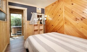 Een slaapkamer met een bed, houten wanden, een raam met gordijnen en uitzicht op de omgeving.