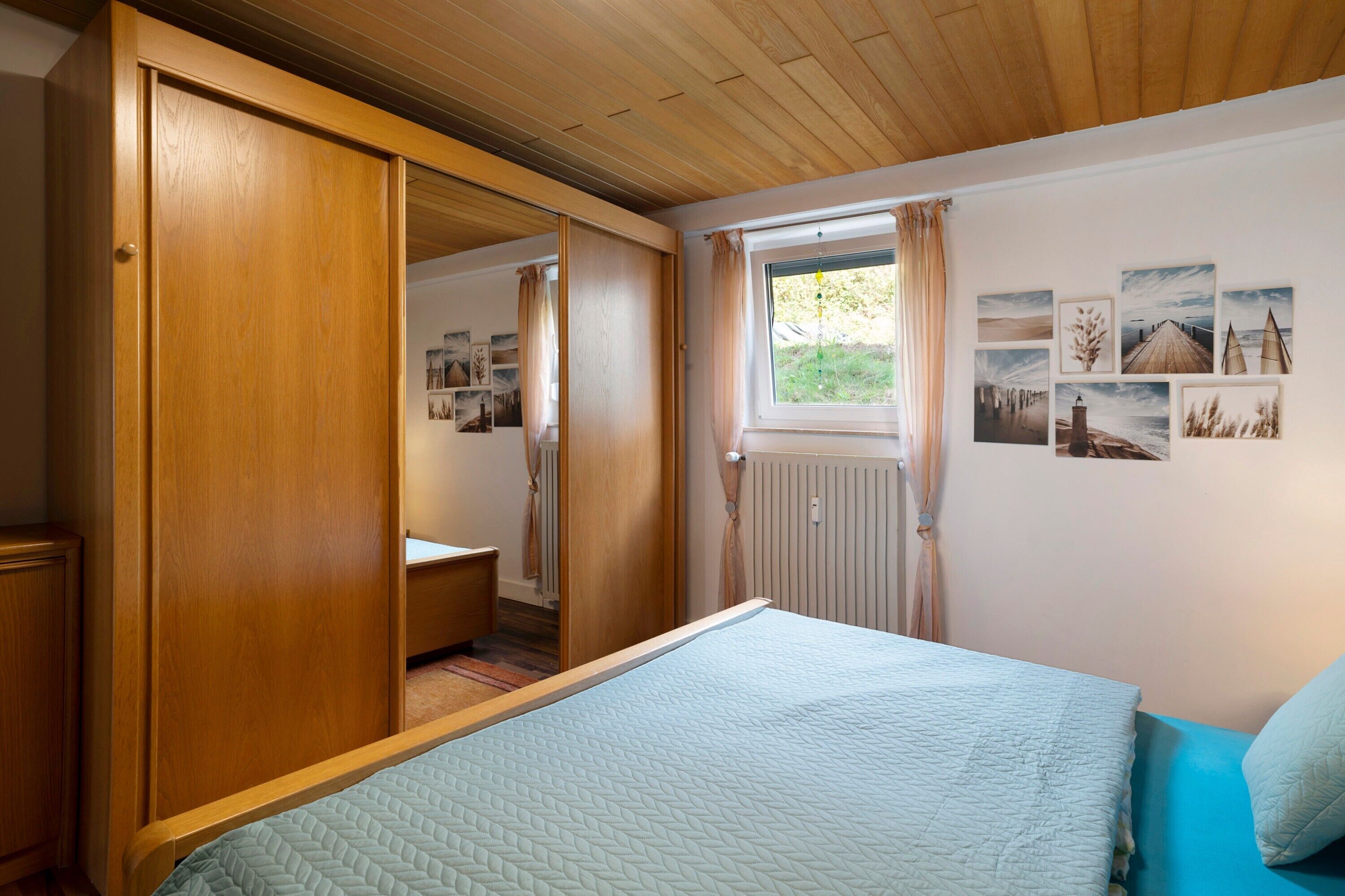A bedroom with a bed, wooden wardrobe, and a window with curtains.