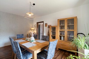 Un'area pranzo con un tavolo in legno, sedie decorate, un lampadario, un mobile con vetri e una pianta in vaso.