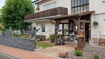 Ein zweistöckiges Gebäude mit Balkon, Sitzgelegenheiten im Freien und Blumentöpfen.