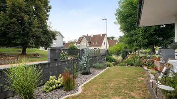 Ein Wohngarten mit Rasen, verschiedenen Pflanzen, einem Zaun und einem Haus im Hintergrund.