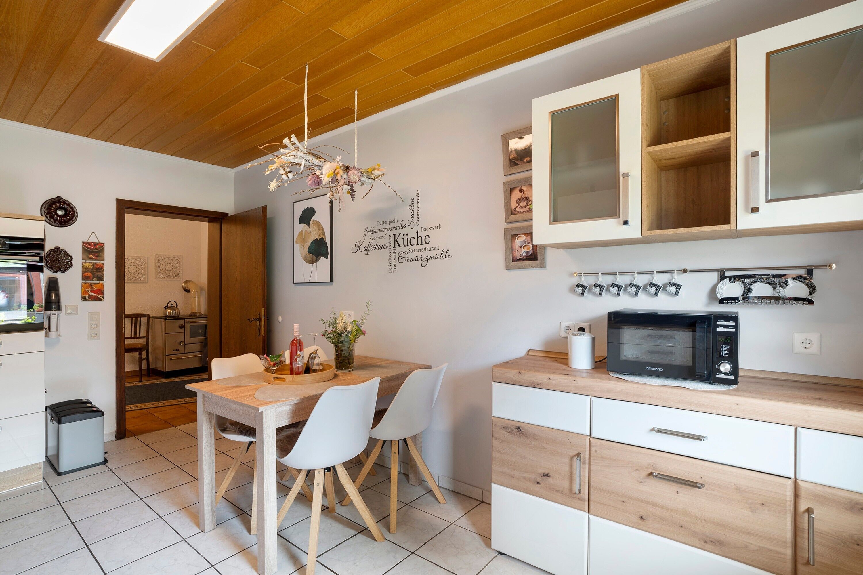 A modern kitchen with wooden cabinets, a dining table with chairs, a microwave, and a chandelier.