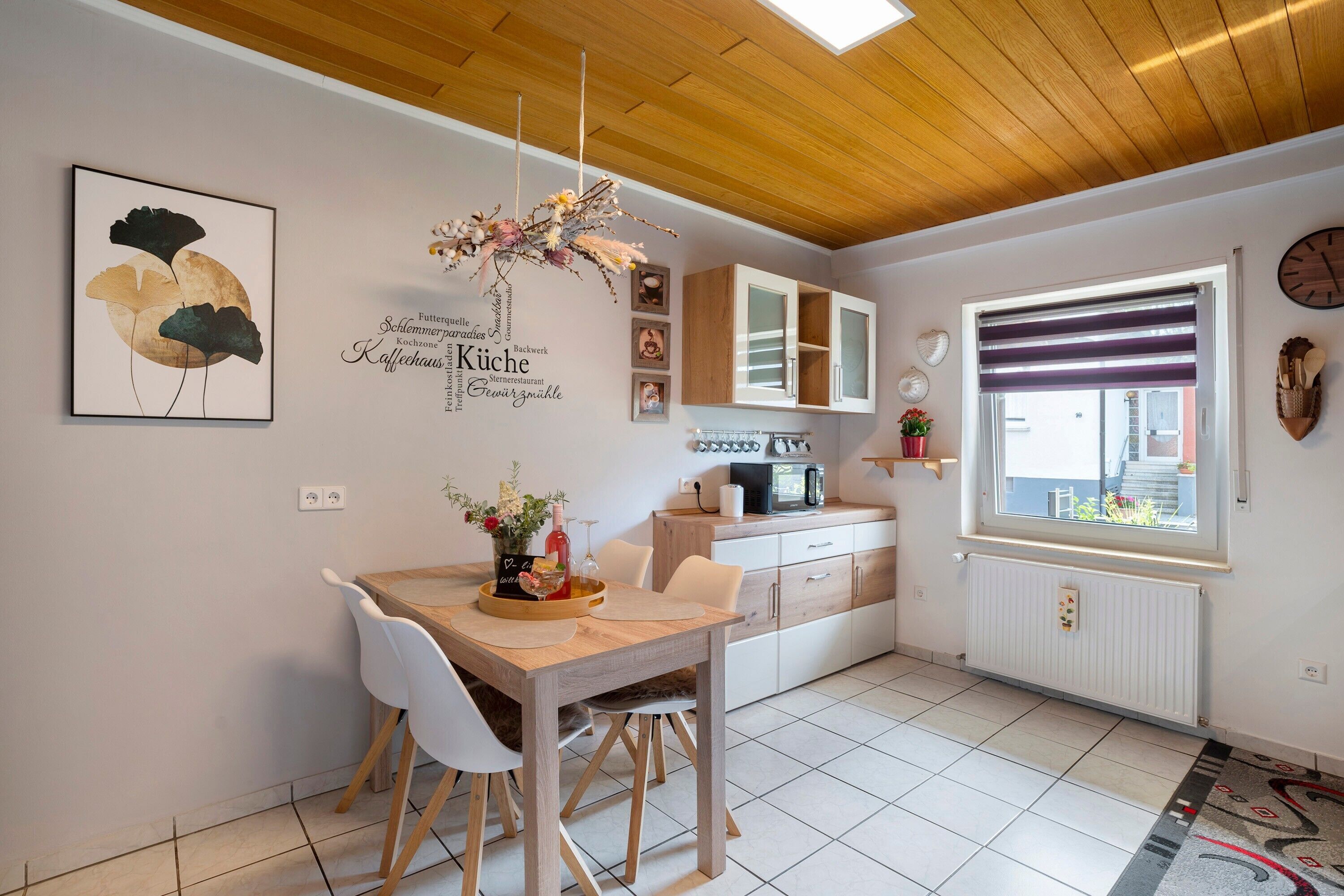 Una cucina moderna con un tavolo di legno, sedie bianche, una lampada a sospensione e una finestra con persiane.