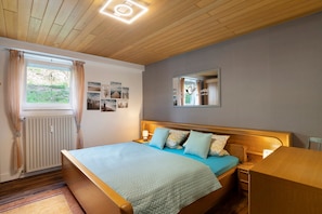 Camera da letto con un letto in legno, un comodino, uno specchio e una finestra con tende.