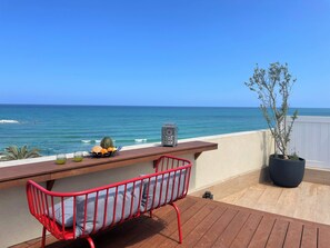 A wooden deck with a red chair and a table with fruits and a lantern. A potted plant is on the right. - 1604 Tel aviv (Tel Aviv)
