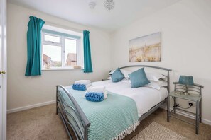Une chambre à coucher avec un lit, des rideaux de couleur turquoise, une fenêtre, une table de chevet avec une lampe et un tableau accroché au mur.