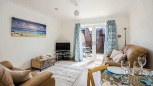 A living room with a sofa, a TV, a dining table set with glasses and plates, and a painting on the wall.