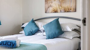 A neatly made bed with white and teal bedding, a framed artwork above it, and a towel with "Zway Holidays" text on the side.