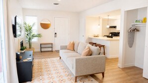 A modern living room with a sofa, a coffee table, and a TV. There is a kitchen area with a counter and a hanging light. - Cozy Studio • DownTown SLC (Salt Lake City)