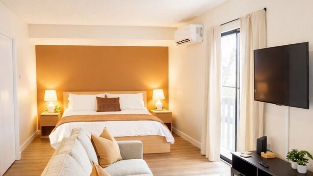 A modern hotel room with a large bed, a sofa, a TV, and a small side table. - Cozy Studio • DownTown SLC (Salt Lake City)