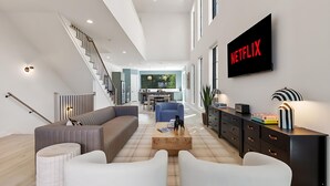A modern living room with a sofa, coffee table, and a TV displaying "NETFLIX". - The Azure - Sleek City Loft + Firepit & Games (Dallas)