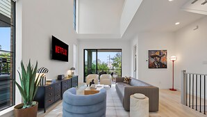 A modern living room with a Netflix sign, a large potted plant, and a sofa. - The Azure - Sleek City Loft + Firepit & Games (Dallas)