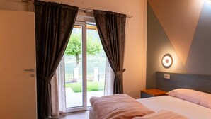 Un dormitori amb un llit, una taula de nit, una làmpada de paret i una porta corredissa de vidre que dona a zona exterior.